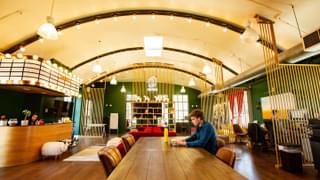 The lobby of a co-working space that is brightly lit. A man is working on a desk.