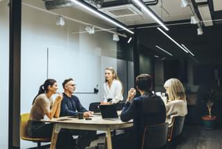 Five people having a meeting in a glass-walled conference room