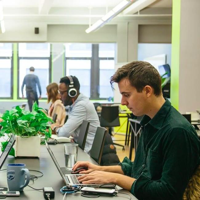 Four people working at desks in a coworking space.